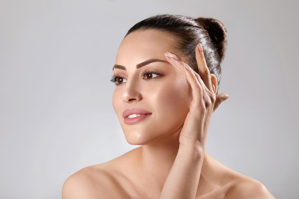 Beautiful young woman with clean perfect skin. Portrait of beauty model with natural nude make up and touching her face. Spa, skincare and wellness. Close up, copyspace.