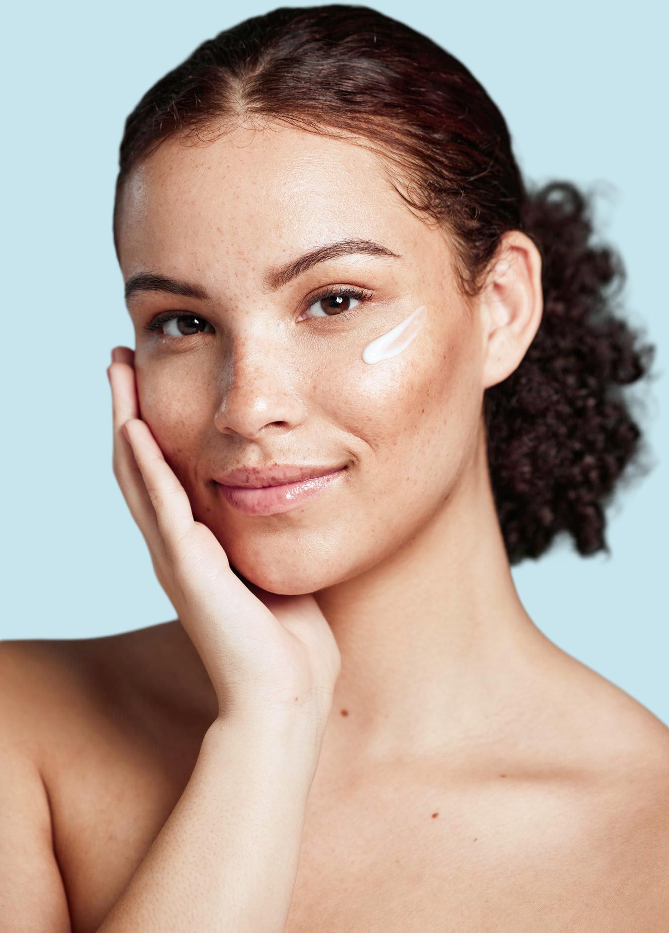 Portrait of a woman with her hand on her cheek and a creme on her other cheek