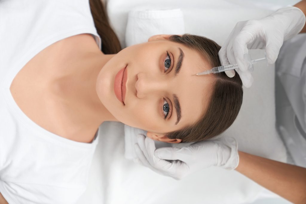 Top view portrait of cute young woman lying on procedure for improvements face skin in beautician. Concept of procedure injection anti-aging skin with professional cosmetics.