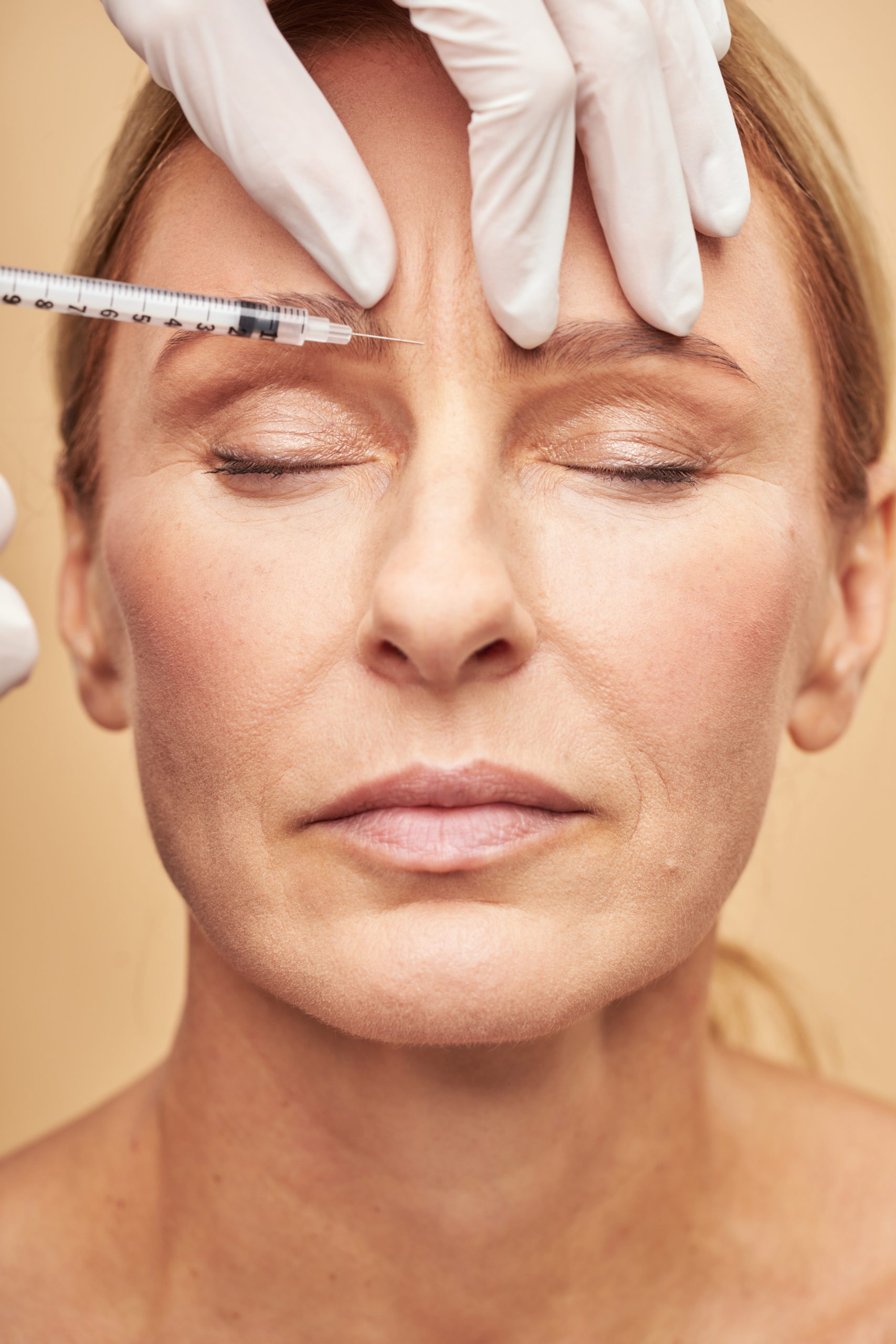 Close up of beautician hands in protective gloves making injection in female forehead. Skin care, anti aging and cosmetology concept