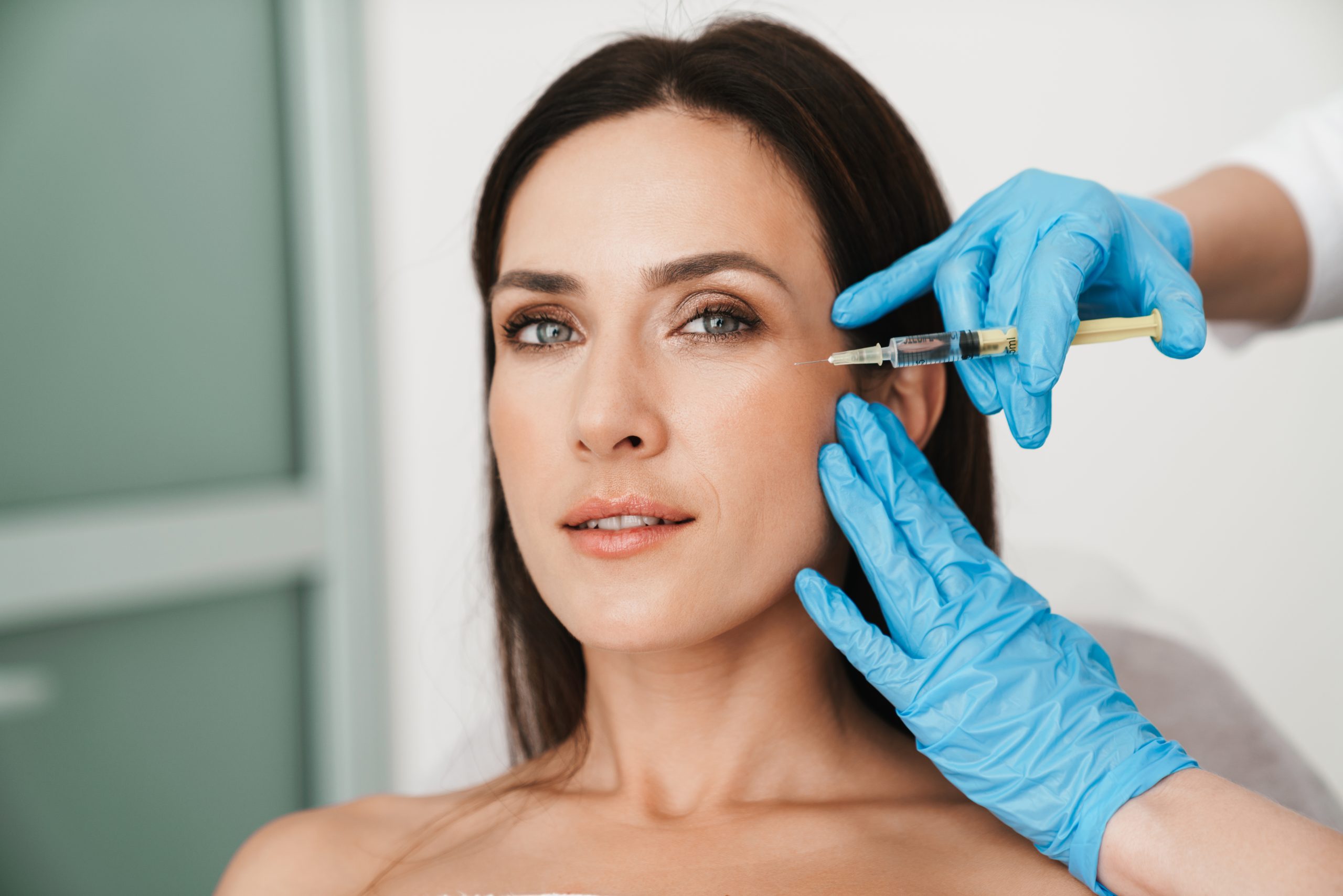 Photo of beautiful woman getting mesotherapy treatment in face by specialist in gloves in beauty salon