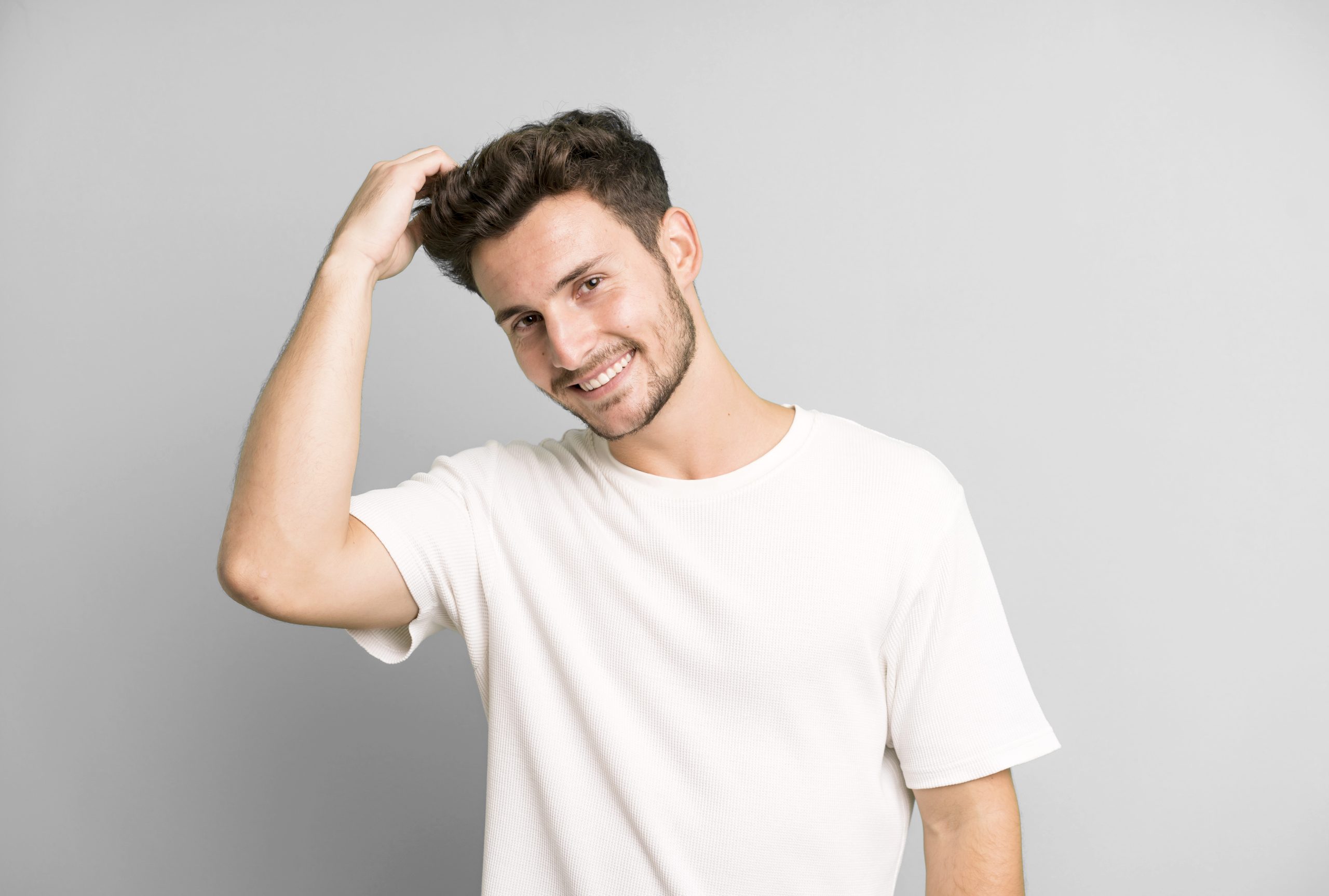 young handsome man smiling cheerfully and casually, taking hand to head with a positive, happy and confident look