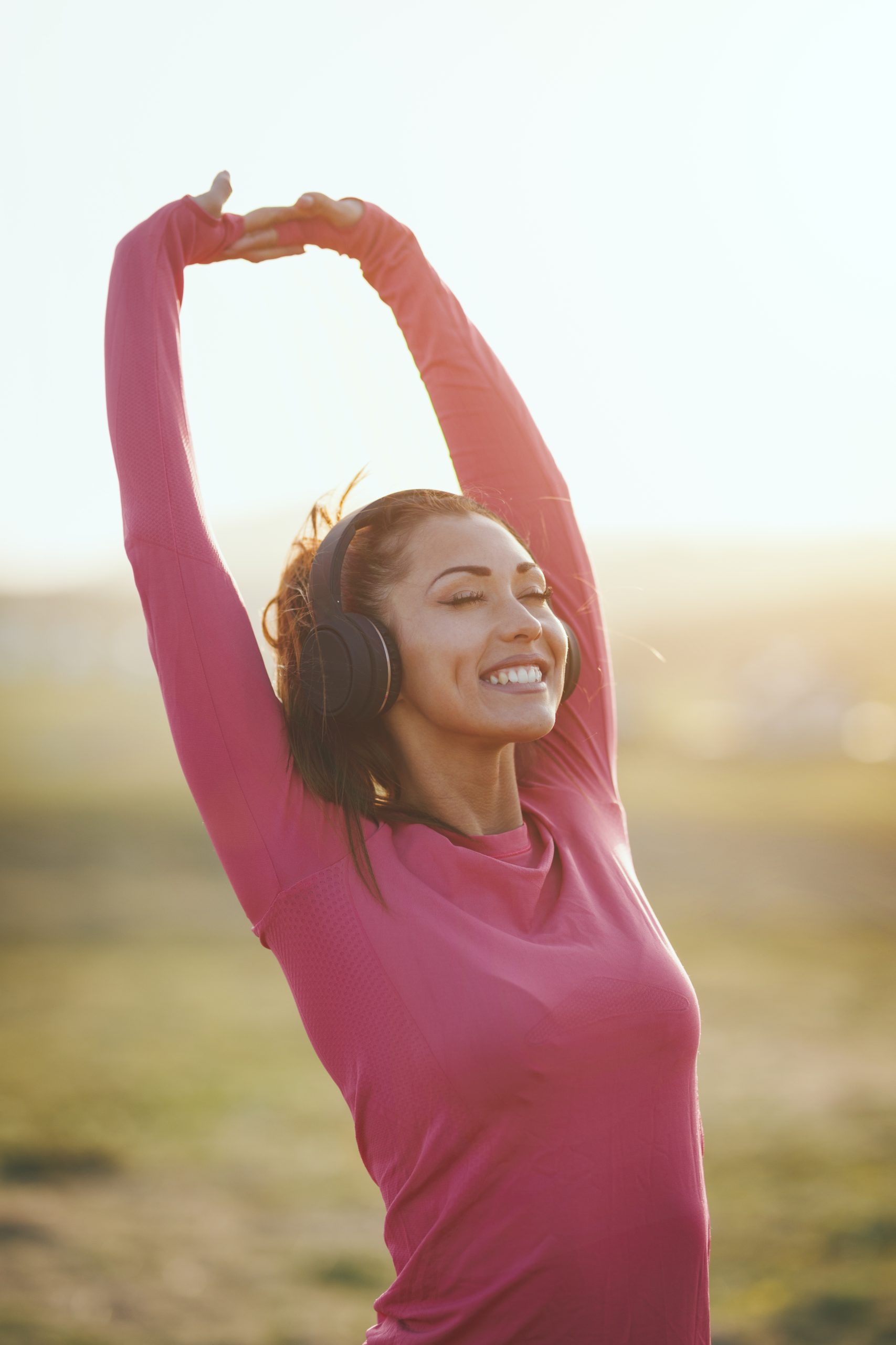 Young beautiful female runner listening to music and warming up before jogging at morning in mountains.