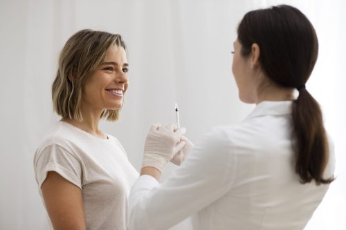 One woman who smiles to the other women who is standing with an injection needle
