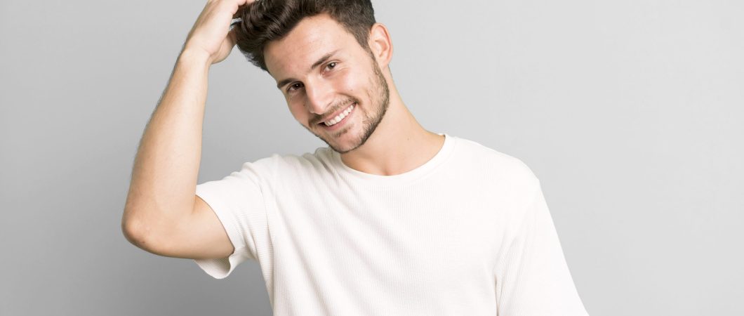 young handsome man smiling cheerfully and casually, taking hand to head with a positive, happy and confident look